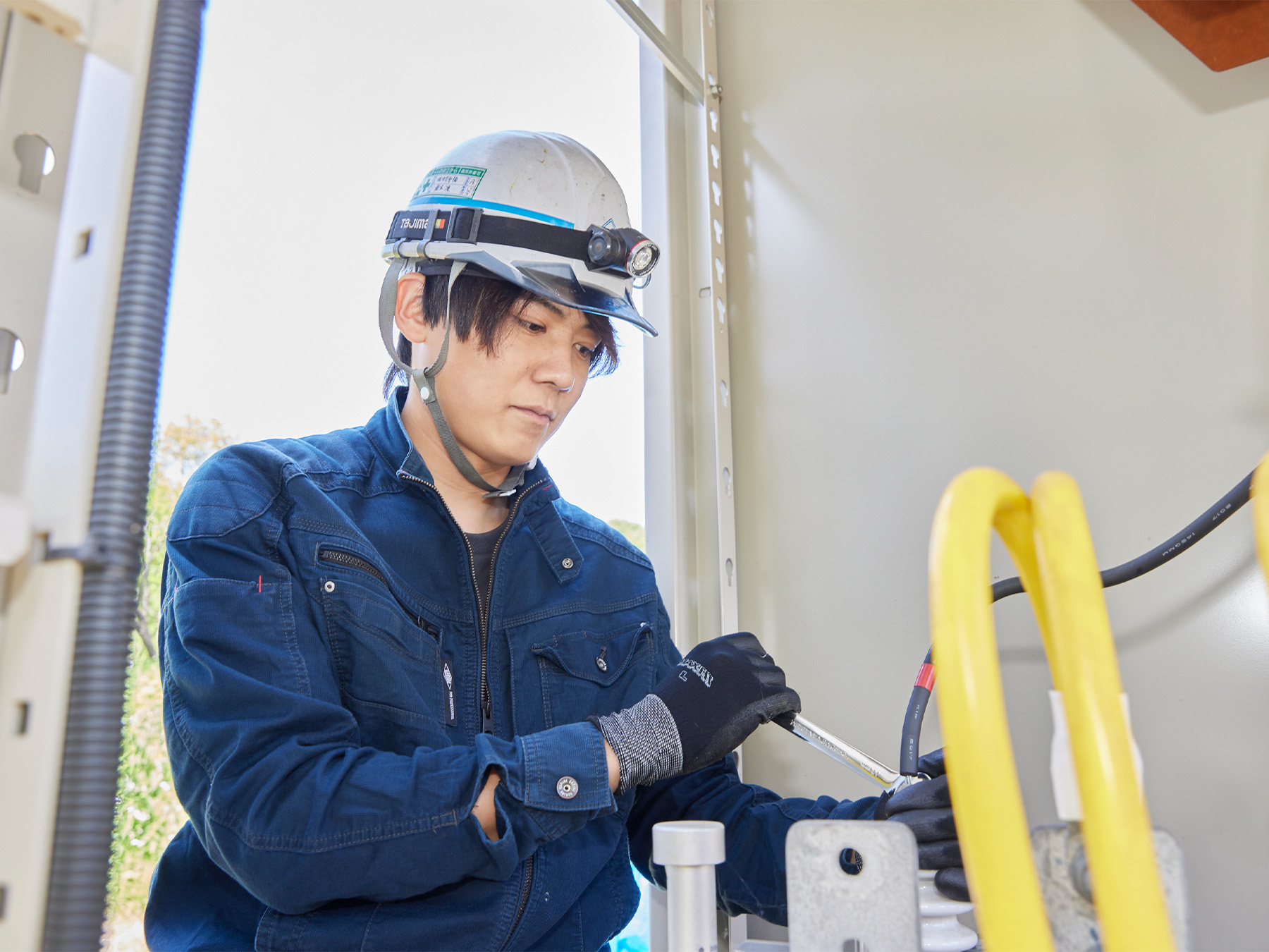作業員が電気設備の内部で工具を使って作業をしている様子