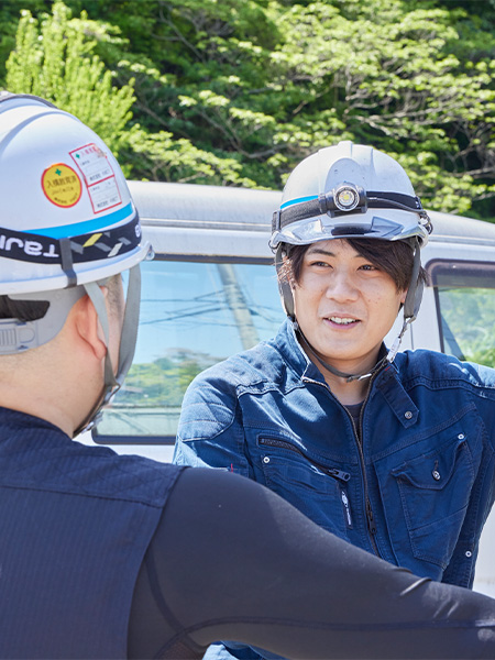 ヘルメットを着用した2人の作業員が屋外で笑顔で会話している様子